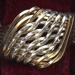 May include: A wide silver and gold woven ring with a textured surface.