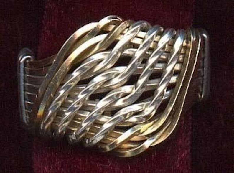 May include: A wide silver and gold woven ring with a textured surface.