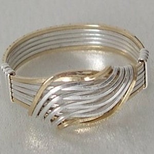 May include: A silver and gold ring with a woven design. The ring is made of multiple strands of wire that are twisted and intertwined to create a unique and intricate pattern.