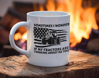 Könnte beinhalten: Eine weiße Keramiktasse mit einem schwarz-weißen Design. Das Design zeigt einen Traktor vor einer amerikanischen Flagge mit dem Text "Sometimes I wonder if my tractors are thinking about me too."