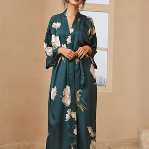 May include: A dark teal satin robe with a floral pattern in white and light pink. The robe has a V-neck, wide sleeves, and a matching belt. The long robe is knee-length and appears to be made of a soft, flowing material.
