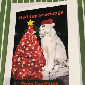 May include: Holiday greeting card featuring a red Christmas tree with a yellow star and a statue of a dog wearing a Santa hat. The card reads "Holiday Greetings" and "From Los Gatos".
