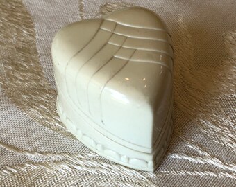 May include: A white heart-shaped trinket box with a raised, geometric design. The box has a hinged lid and a smooth, glossy finish.