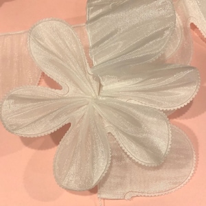 May include: White tulle flower with a scalloped edge. The flower is made of multiple layers of tulle and is gathered in the center.