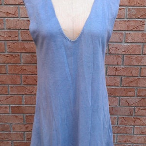 Peut inclure: Robe sans manches bleu clair avec un col en V profond, présentée sur un mannequin. La robe a un design simple et fluide et est faite d'un tissu doux. Le mannequin est sur un support en métal noir, devant un mur de briques.
