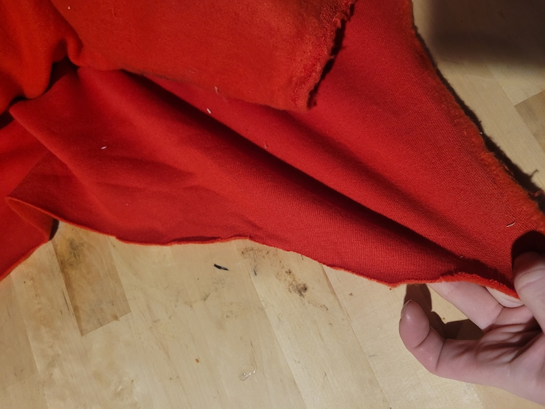 Peut inclure: Gros plan sur un tissu rouge vif avec un bord brut et inachev&eacute;. Le mat&eacute;riau est pli&eacute;, r&eacute;v&eacute;lant sa texture et sa couleur. Le tissu est probablement un textile utilis&eacute; pour l'habillement ou l'artisanat.