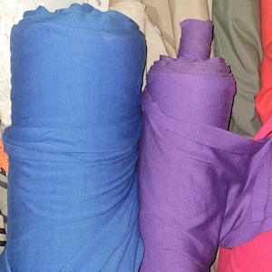 Peut inclure: Deux rouleaux de tissu, l'un bleu et l'autre violet, sont empilés l'un sur l'autre. Le tissu est enroulé serré et semble doux et lisse.