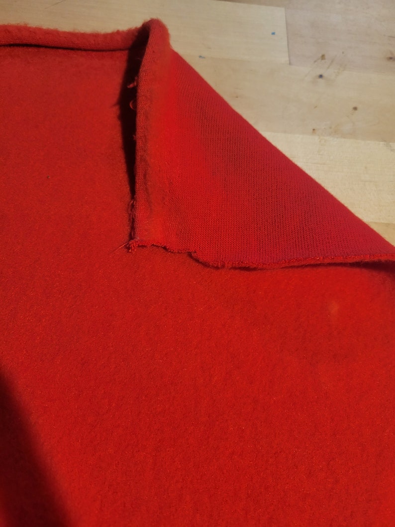 Peut inclure: Un tissu rouge vif, peut-&ecirc;tre du feutre ou un mat&eacute;riau similaire, est partiellement pli&eacute;, r&eacute;v&eacute;lant sa surface textur&eacute;e. Les bords pr&eacute;sentent un aspect brut et inachev&eacute;. Le tissu est d'un rouge uni et brillant.
