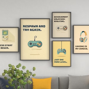May include: A collection of framed art prints with gaming-themed illustrations. The prints feature game controllers, headphones, and text like "Respawn and Try Again" and "Gaming is My Cardio." The color palette includes beige, blue, and yellow.