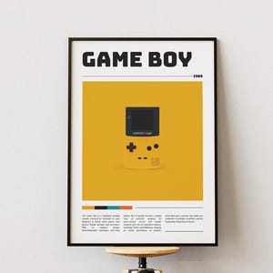 Puede incluir: Póster enmarcado con una consola Game Boy amarilla sobre un fondo amarillo. Las palabras "GAME BOY" están en la parte superior en letras negras en negrita, con "1989" debajo. El póster tiene un marco negro y se muestra en un soporte de madera.