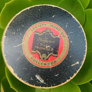May include: Vintage Max Factor's Society Make-Up Face Powder compact with a black and gold design and the text "Max Factor's Face Powder Hollywood" on the front.