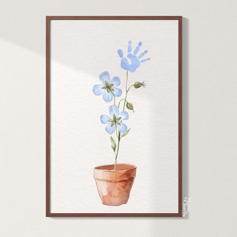 May include: A watercolor painting of a blue flower in a terracotta pot with a blue handprint above it. The painting is framed in a brown frame and signed "Mama & Charlie".