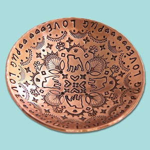 May include: A copper bowl with an intricate design featuring paw prints, hearts, and the words "Love Pug Love" repeated around the rim.