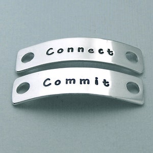 May include: Two silver metal tags with holes for attaching to a shoe or bag. The top tag says "Connect" and the bottom tag says "Commit".