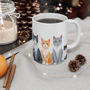 以下が含まれることがあります： 白いセラミック製のマグカップに、4匹の猫のデザインが施されています。猫は、グレーのトラ猫、白黒の猫、オレンジのトラ猫、グレーの猫です。マグカップには暗い色の液体が注がれており、蒸気が上がっています。