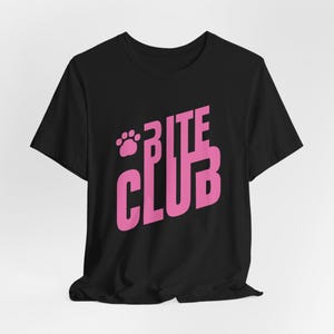 Può includere: T-shirt nera con la scritta "BITE CLUB" in rosa acceso, accompagnata da un'impronta di zampa. Il testo è in grassetto e la maglietta è realizzata in un materiale morbido.