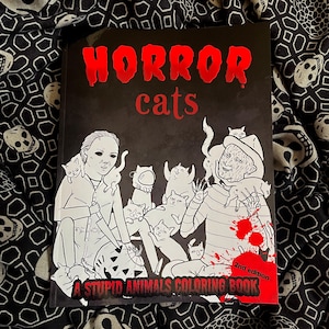 May include: A black coloring book titled "HORROR cats" with red lettering. The cover features illustrations of horror movie characters with cats. The text "A STUPID ANIMALS COLORING BOOK" is at the bottom, with "2nd edition" in the corner.