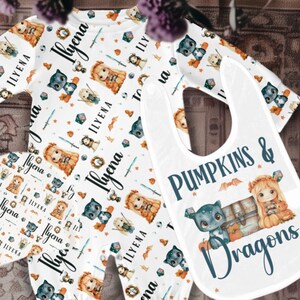 May include: A white baby onesie with a repeating pattern of a girl with a sword, a black cat, and the name "Ilyena". A white bib with the text "Pumpkins & Dragons" and a black cat and girl with a pumpkin is also included.