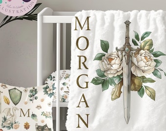 May include: White baby blanket with a floral design and a sword. The blanket has the name "MORGAN" spelled out vertically in gold letters.
