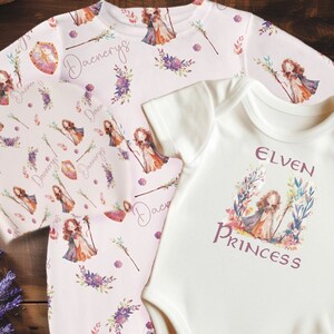 May include: Two baby onesies, one pink with a floral pattern and the text "Daenerys" and one white with the text "Elven Princess".