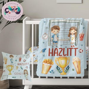 May include: A blue and white personalized blanket with a soccer theme. The blanket features a boy and girl playing soccer, a soccer goal, a trophy, popcorn, french fries, and a soda. The name "HAZLITT" is written in red letters on the blanket.