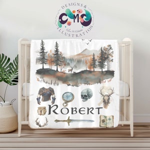 May include: A white baby blanket featuring a watercolour forest scene, a compass, a skull, a deer skull, a sword, a book, a bag, and armour. The name "Robert" is written in black lettering.
