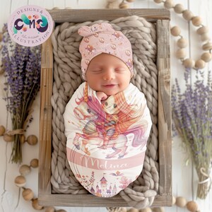 May include: A pink and white swaddle with a unicorn and princess illustration. The swaddle has the name "Melina" printed on it. A pink and white knotted hat with floral designs is on the baby's head.