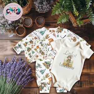 May include: A set of baby clothes featuring a whimsical forest theme. The set includes a long-sleeved onesie and a short-sleeved bodysuit. The onesie has a repeating pattern of gnomes, mushrooms, and foliage. The bodysuit reads "Littlest Wanderer".