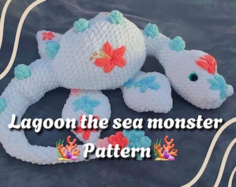 Könnte beinhalten: Weißes gehäkeltes Seeungeheuer mit blauen und rosa Blumendetails. Das Ungeheuer liegt auf einer welligen, gemusterten Oberfläche. Der Text "Lagoon the sea monster Pattern" befindet sich unter dem Ungeheuer.