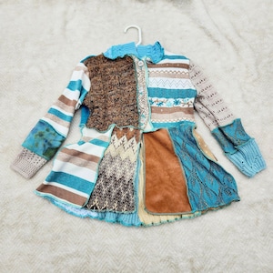 May include: A patchwork jacket with a variety of textures and patterns. The jacket features brown, blue, and white stripes, knit sections, and a faux suede panel. It has a round collar and button closure.