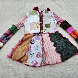 Könnte beinhalten: Eine bunte Patchwork-Jacke mit einem einzigartigen Design. Die Jacke hat einen Mix aus Stoffen, darunter Blumenmuster, Punkte und Strickabschnitte. Die Ärmel sind mehrfarbig und der Rock hat einen gewellten Rand. Die Jacke ist zugeknöpft und hat einen Kragen.
