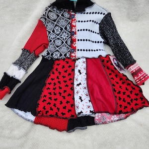 Könnte beinhalten: Ein Patchwork-Kleid mit einer Vielzahl von Mustern und Texturen. Das Oberteil hat einen schwarzen Rollkragen und eine Mischung aus roten, schwarzen, weißen und gemusterten Stoffen. Der Rock hat ein ausgestelltes Design mit Hunde- und Blumenmustern.