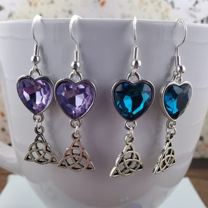 May include: Three pairs of silver heart-shaped earrings with a Celtic knot design. The earrings feature purple, blue, and teal crystal stones.