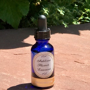 Puede incluir: Una botella de vidrio azul con un gotero y una etiqueta dorada que dice "Sublime Flower Essences" y "SANDWOTH".