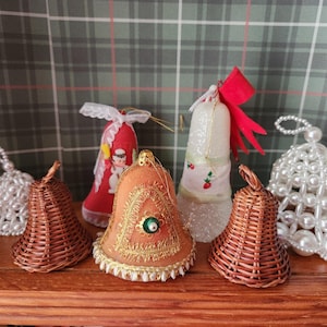 May include: A collection of Christmas bell ornaments in various styles. Includes woven wicker bells, beaded bells, and bells with fabric and decorative accents. The color palette includes brown, red, white, and gold, with a plaid background.