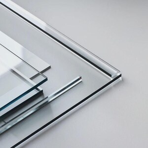 Puede incluir: Una pila de varias láminas rectangulares de acrílico transparente con bordes lisos y pulidos. Los paneles transparentes están superpuestos en ángulos ligeros, mostrando su grosor y la alta calidad del material con líneas nítidas y limpias.