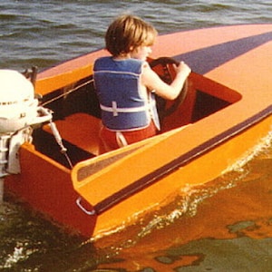 May include: A small orange and black boat with a white outboard motor. A child is driving the boat.
