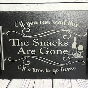 May include: Black slate serving tray with silver handles. The tray has a white inscription that reads "If you can read this The Snacks Are Gone It's time to go home". The inscription is surrounded by decorative swirls. A bottle of wine and a glass of wine are depicted next to the inscription.