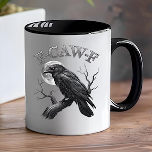 May include: White ceramic mug with a black interior and handle. The mug features a detailed illustration of a black raven perched on a branch in front of a full moon. The text "F-CAW-F" is arched above the raven.