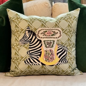 May include: A green and white pillow with a zebra and a floral design. The zebra is sitting on a yellow and white pedestal.