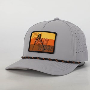 May include: A gray trucker hat with a black and orange rope detail around the brim. The hat has a patch on the front with the text "TWO EIGHT THREE" and a compass design in orange, yellow, and brown.