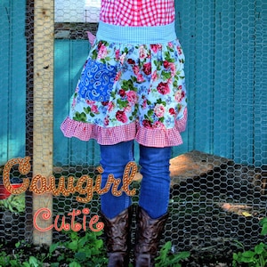 May include: A blue and white floral print apron with a red and white gingham trim and a blue paisley pocket. The apron is worn over a red and white gingham shirt and blue jeans. The person is wearing cowboy boots.