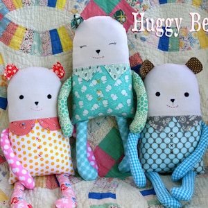 May include: Three handmade plush huggable bears with different colored polka dot fabric. The bears are sitting on a patchwork quilt with the text "Huggy Bears" in the top right corner.