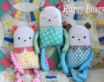 May include: Three handmade plush huggable bears with different colored polka dot fabric. The bears are sitting on a patchwork quilt with the text "Huggy Bears" in the top right corner.