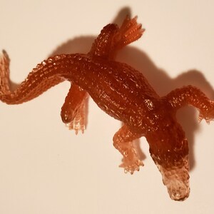 May include: A small, brown, rubber alligator toy. The toy is translucent and has a textured surface.
