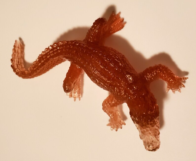 May include: A small, brown, rubber alligator toy. The toy is translucent and has a textured surface.