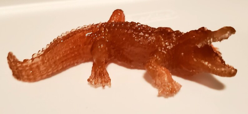 May include: A brown, translucent alligator figurine with a textured surface and an open mouth.