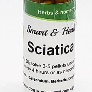 May include: A clear glass bottle with a black cap, filled with small, round, brown pellets. The label reads "Sciatica" and lists ingredients and instructions. The bottle is labeled "Herbs & homeo's".