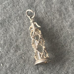 Puede incluir: Un charm de plata con forma de pequeña botella de vidrio transparente con una jaula de plata alrededor. La botella tiene una tapa de plata y un lazo de plata en la parte superior para sujetarlo a una cadena.