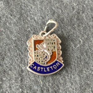 May include: Silver charm with a blue and orange enamel design of a coat of arms with the word "CASTLETON" on a blue banner.